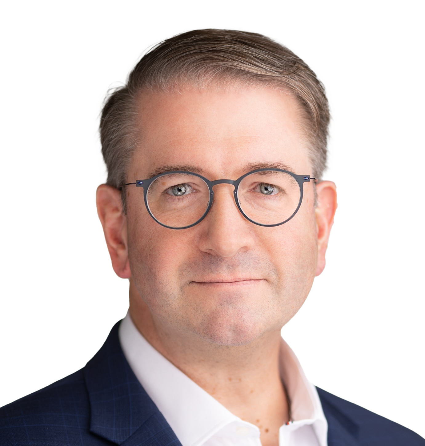 Professional headshot of Chris Shelton with short light brown hair, wearing round eyeglasses, a navy blue suit, and a white shirt, posing against a plain light background.