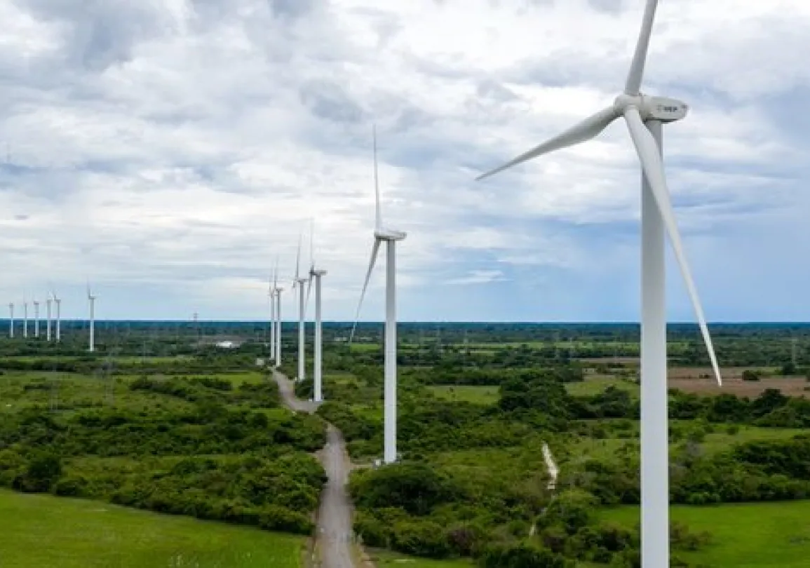 A row of wind turbines in a green landscape under a cloudy sky, generating renewable energy.