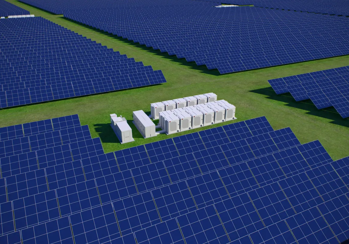 Aerial view of a large solar farm with rows of blue solar panels on green grass. In the center, there are several white rectangular structures, likely housing equipment.