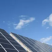 Solar panels angled towards a clear blue sky with a few clouds.