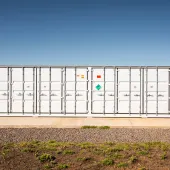 Large white shipping container with multiple doors and hazard signs, situated on a concrete platform under a clear blue sky.