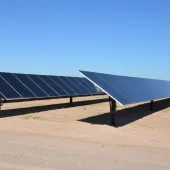 Rows of solar panels in a desert landscape under a clear blue sky.