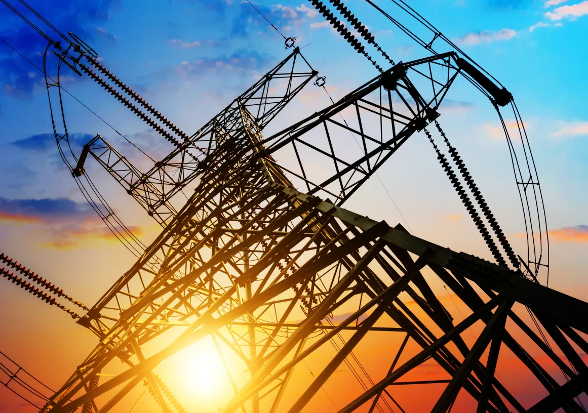 A silhouette of an electricity pylon against a vibrant sunset sky, with hues of orange, pink, and blue.