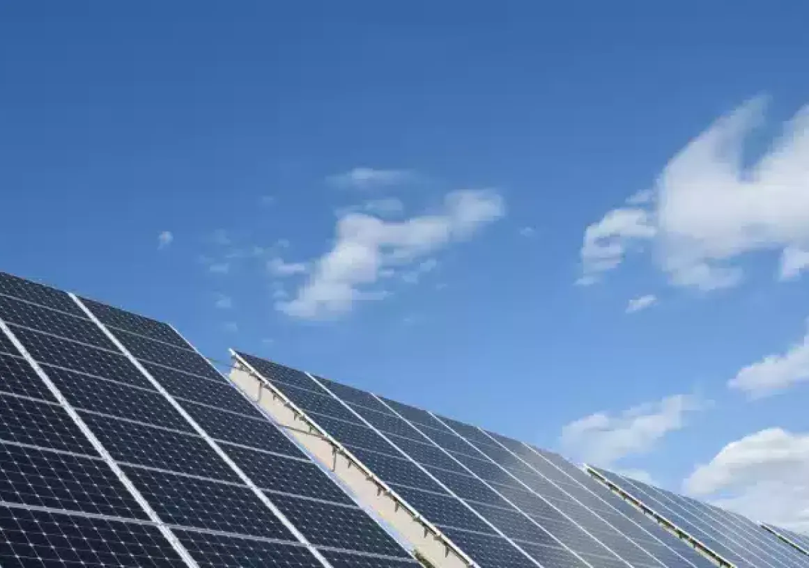 Solar panels angled towards a clear blue sky with a few clouds.