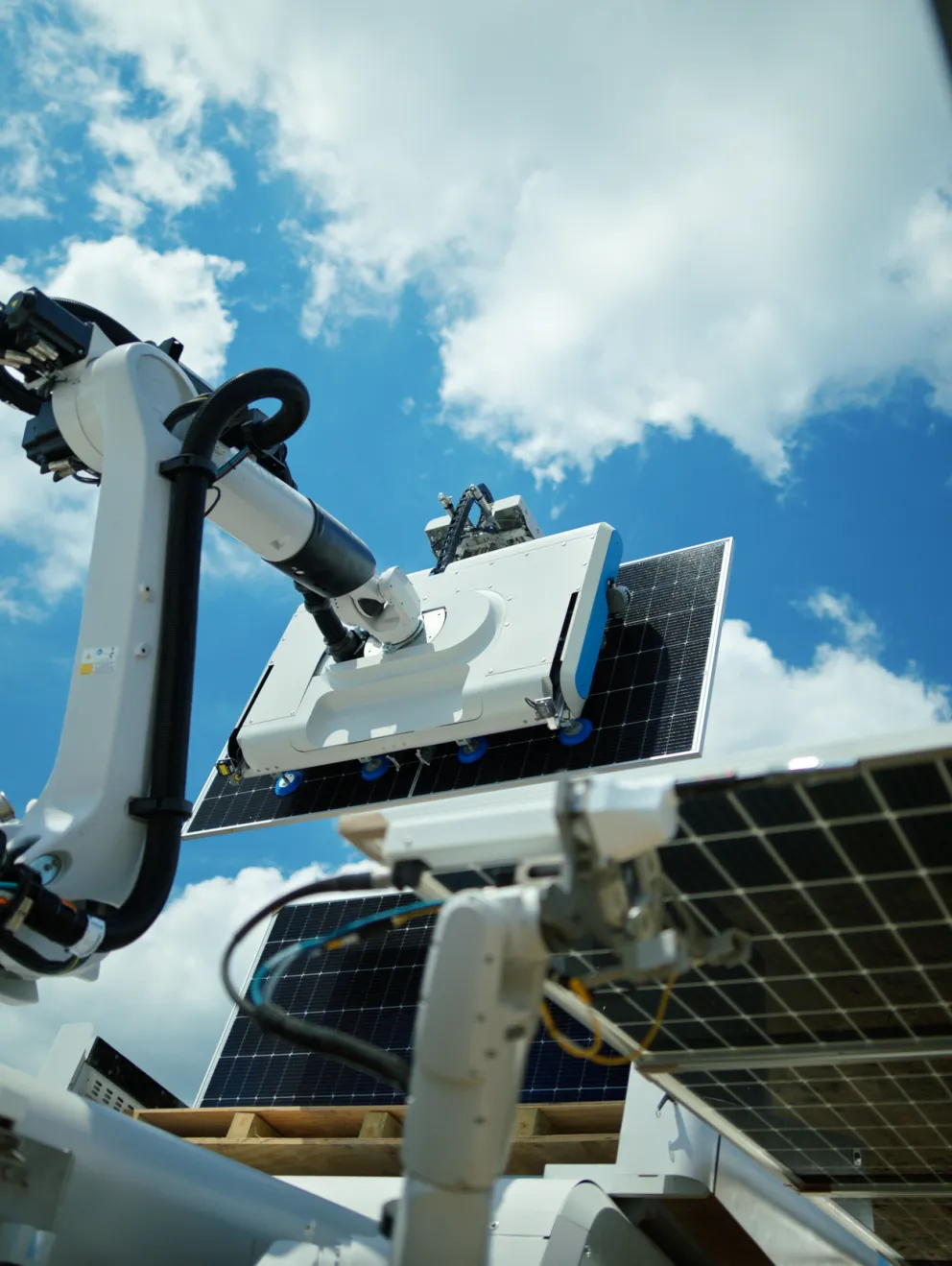 Robotic arm with a cleaning device on a solar panel against a blue sky with clouds.