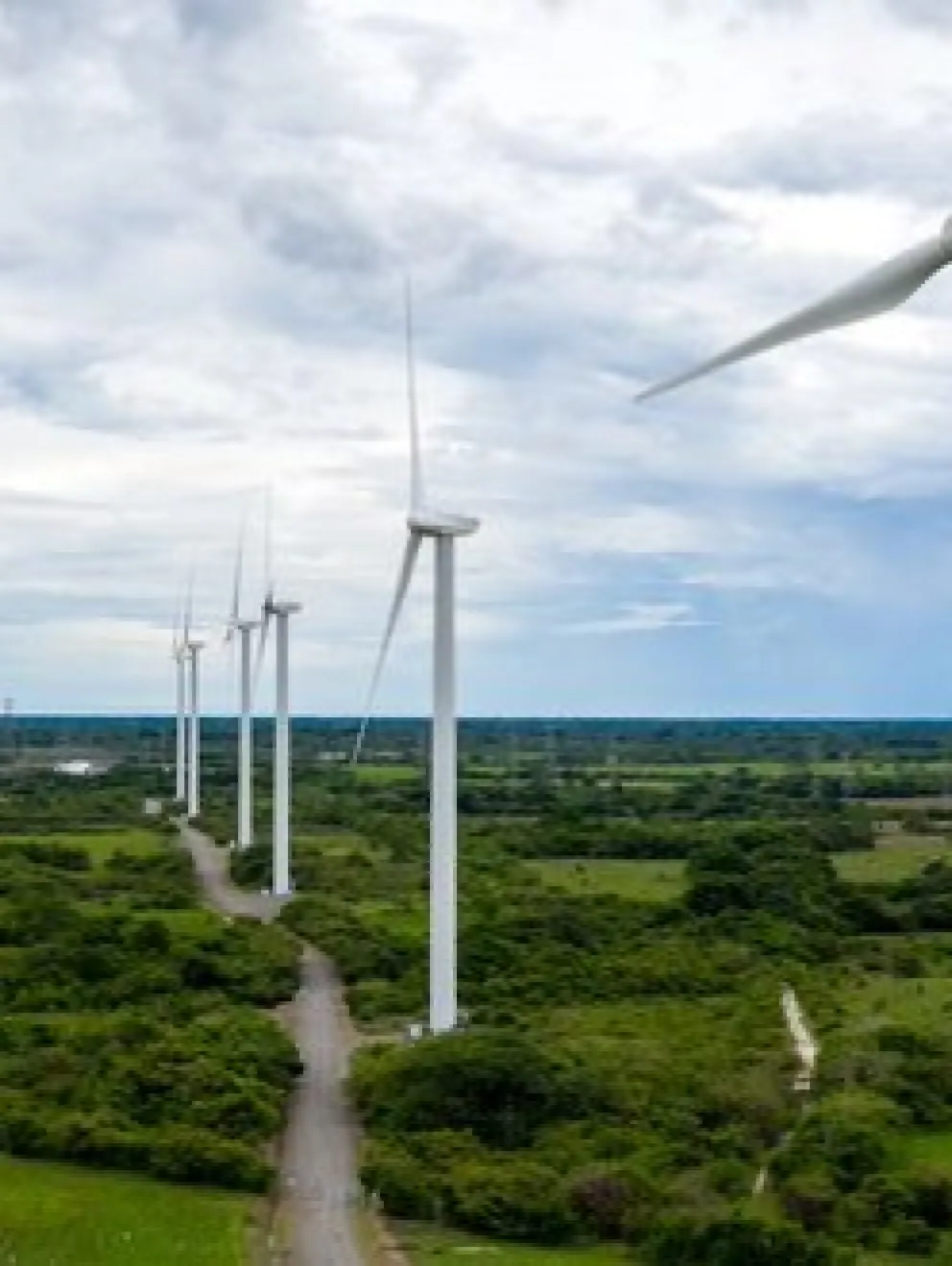 A row of wind turbines in a green landscape under a cloudy sky, generating renewable energy.