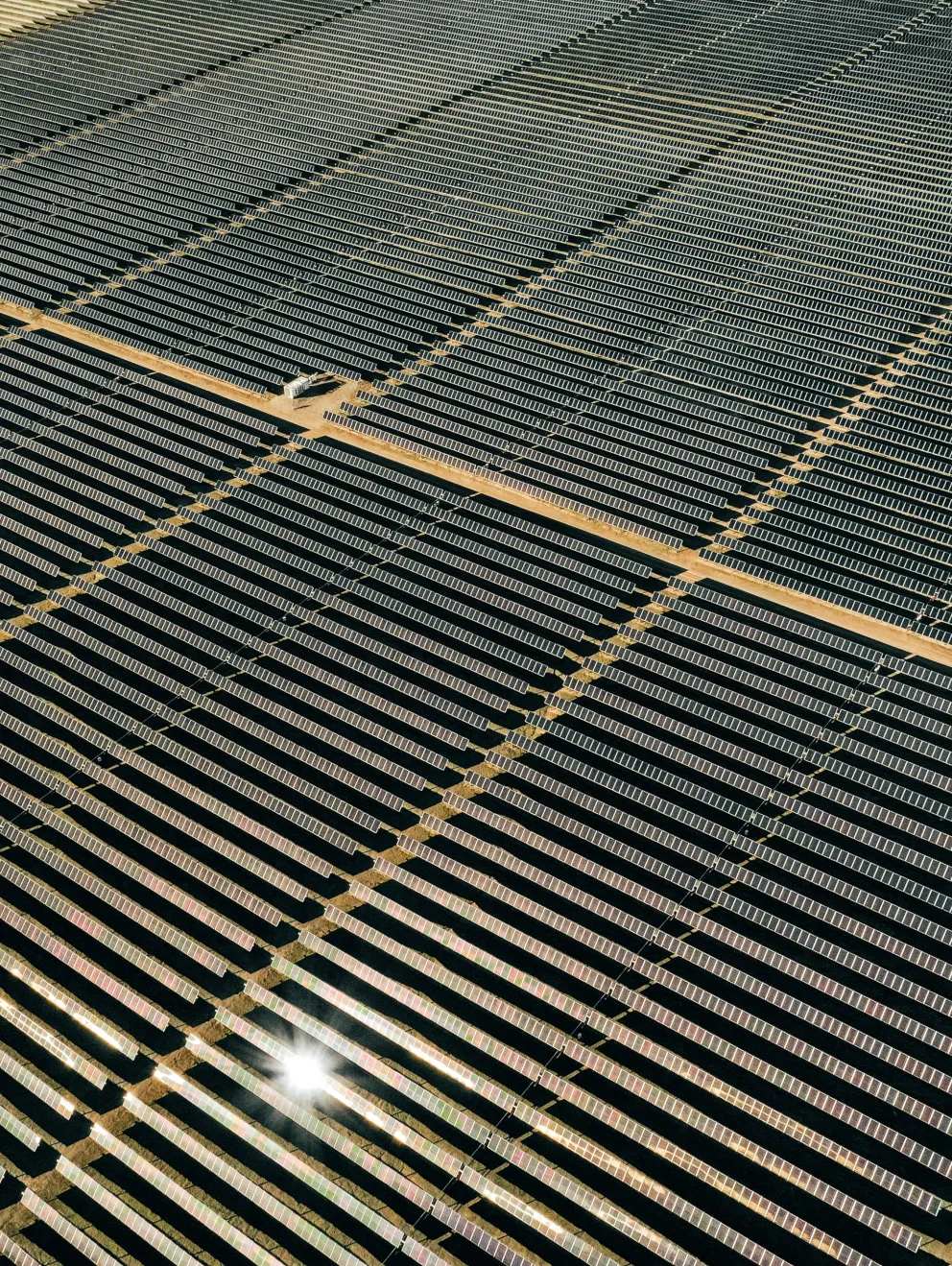 Aerial view of a large solar farm with rows of solar panels arranged in a grid pattern, reflecting sunlight.