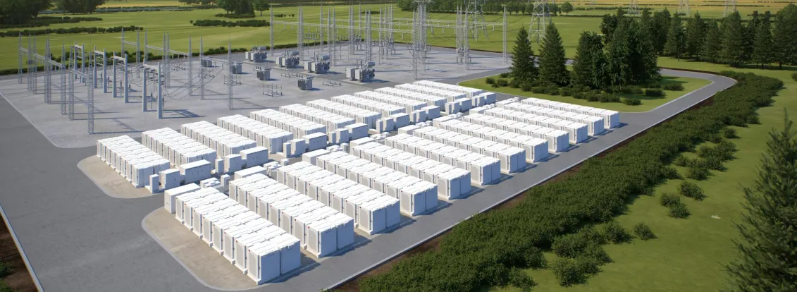 A large outdoor energy storage facility with numerous white battery units arranged in rows. Adjacent to the battery units are electrical substations with metal structures and power lines. The facility is surrounded by green fields and trees, with mountains visible in the background under a clear blue sky.