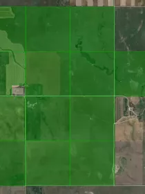 Aerial view of farmland with large green fields divided by grid lines, surrounded by patches of brown and tan land.