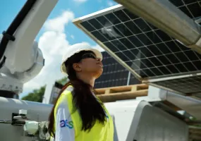 A person wearing a hard hat and safety vest inspects solar panels under a clear blue sky.