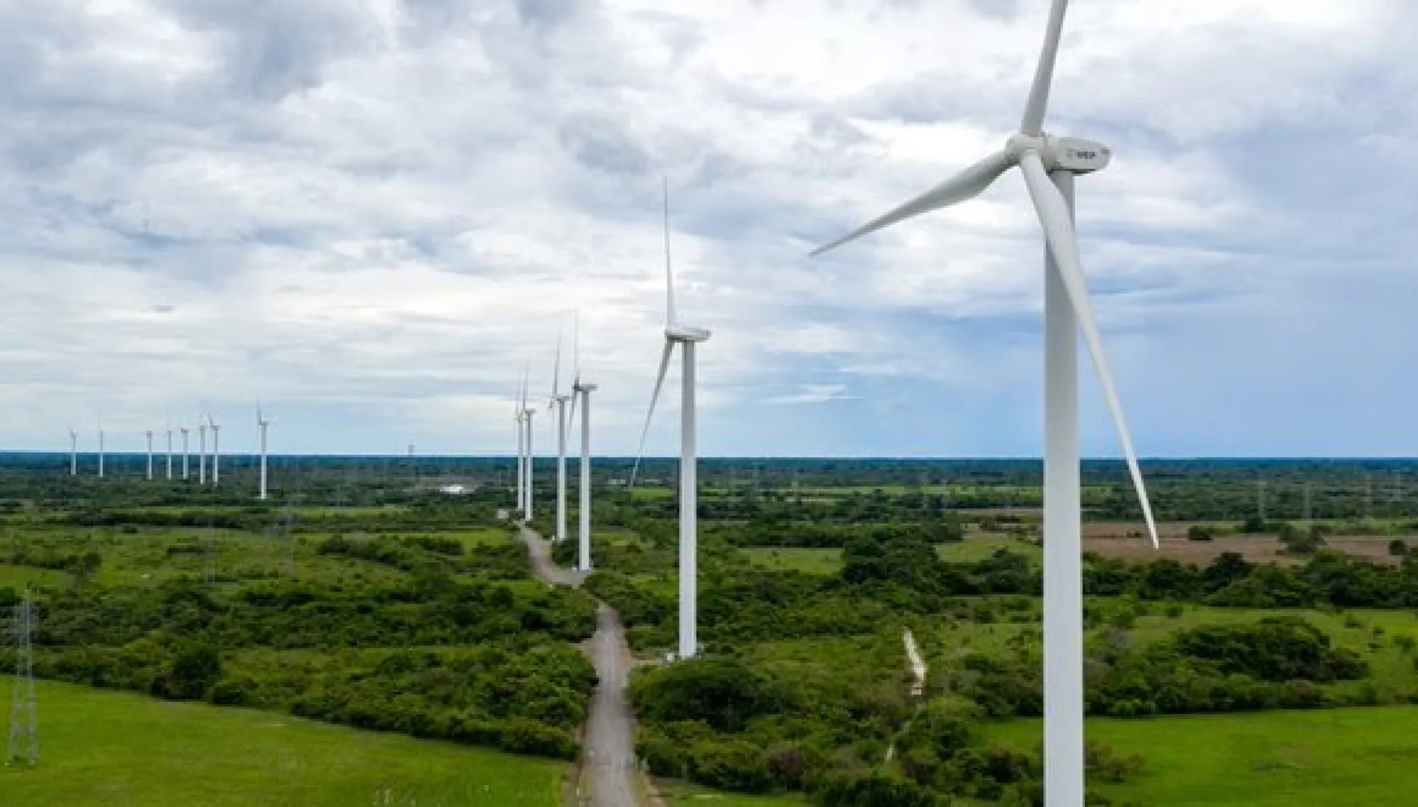 A row of wind turbines in a green landscape under a cloudy sky, generating renewable energy.