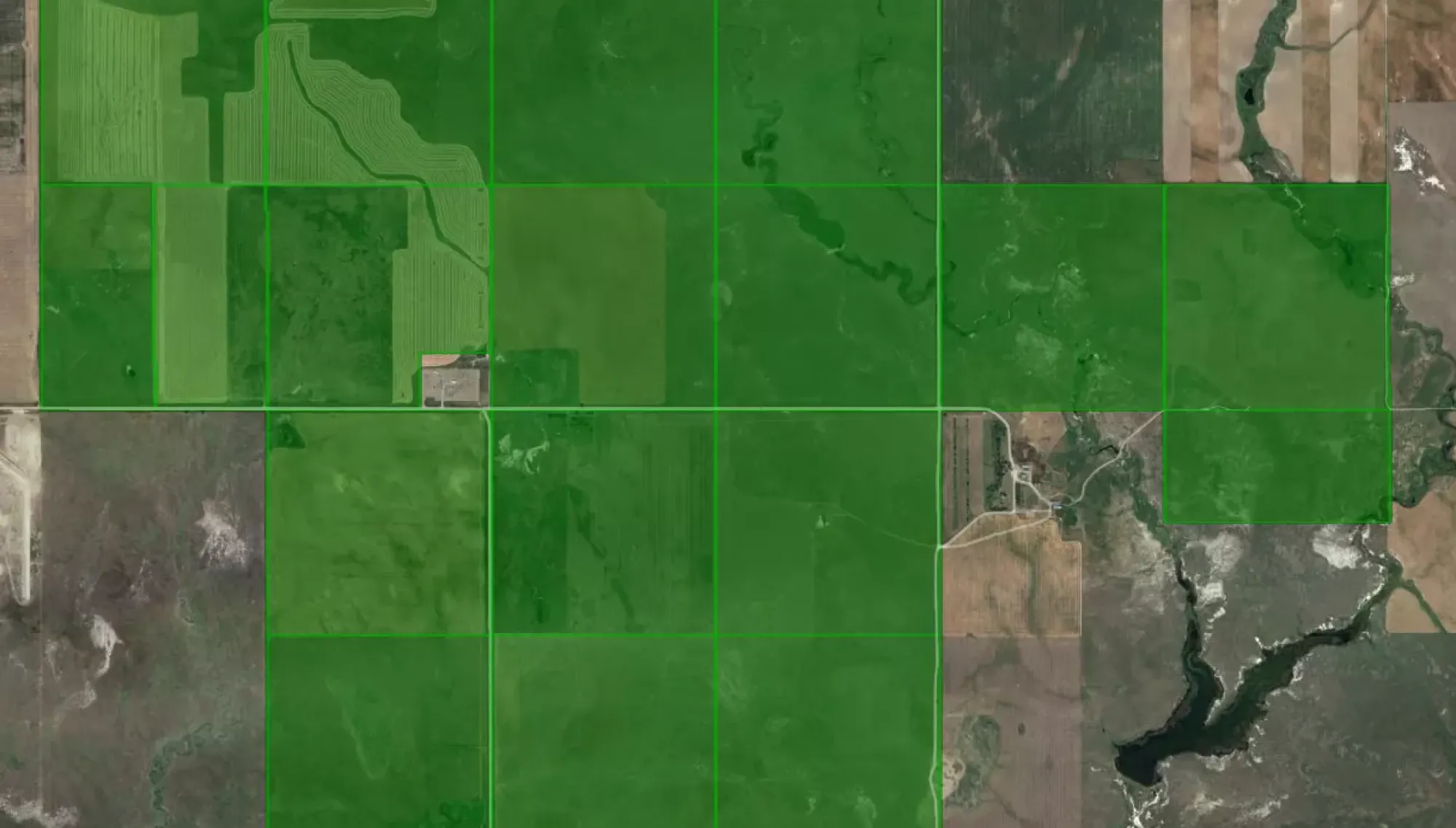 Aerial view of farmland with large green fields divided by grid lines, surrounded by patches of brown and tan land.