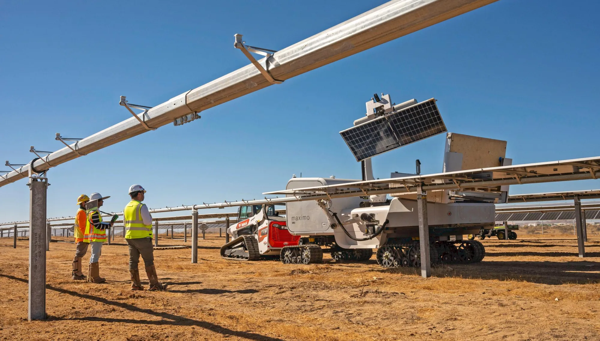 Three workers in safety gear stand near a solar panel installation site with a robotic vehicle on a sunny day.