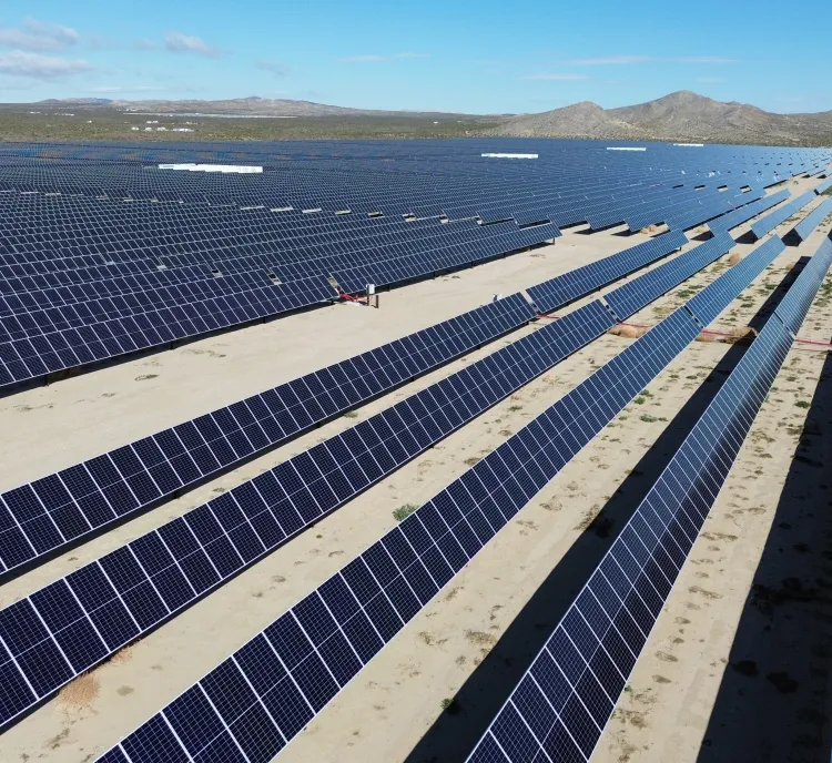 Aerial view of a large solar farm with rows of solar panels stretching across a desert landscape under a clear blue sky.