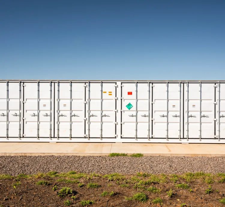 Large white shipping container with multiple doors and hazard signs, situated on a concrete platform under a clear blue sky.