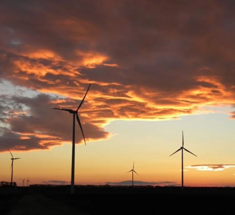 Silhouetted wind turbines under a dramatic sunset sky with orange and purple clouds.