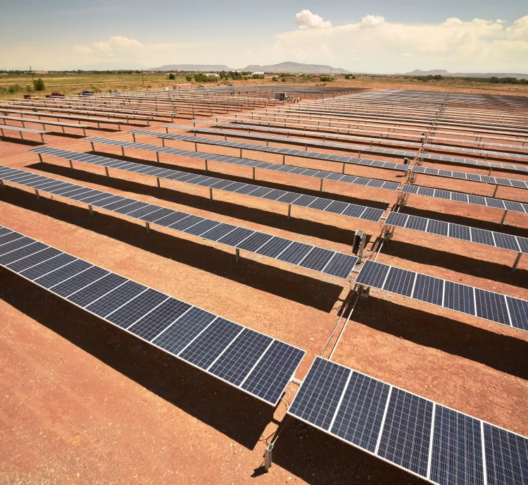 Aerial view of a large solar farm with rows of solar panels on a dry, barren landscape under a clear sky.