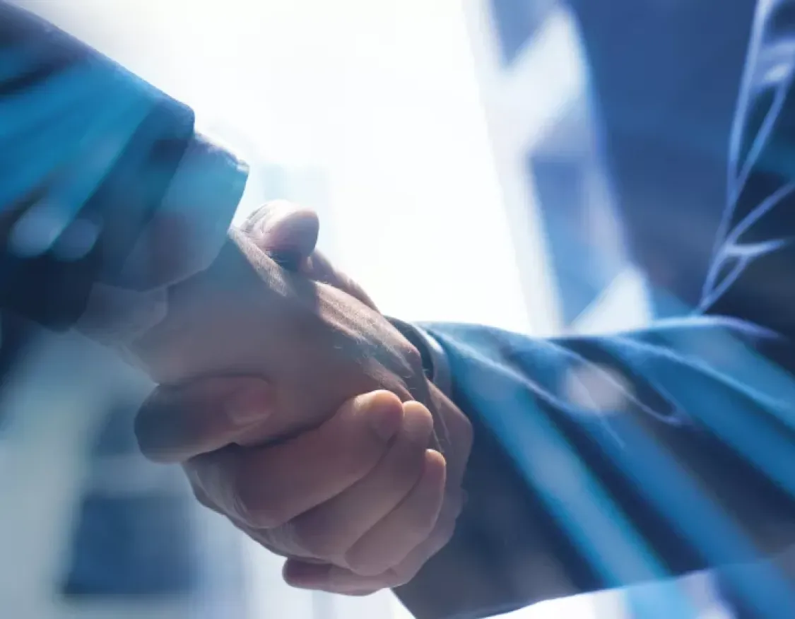 Close-up of a handshake between two people wearing business suits. The background features abstract blue streaks and a blurred cityscape, suggesting a business or professional setting.