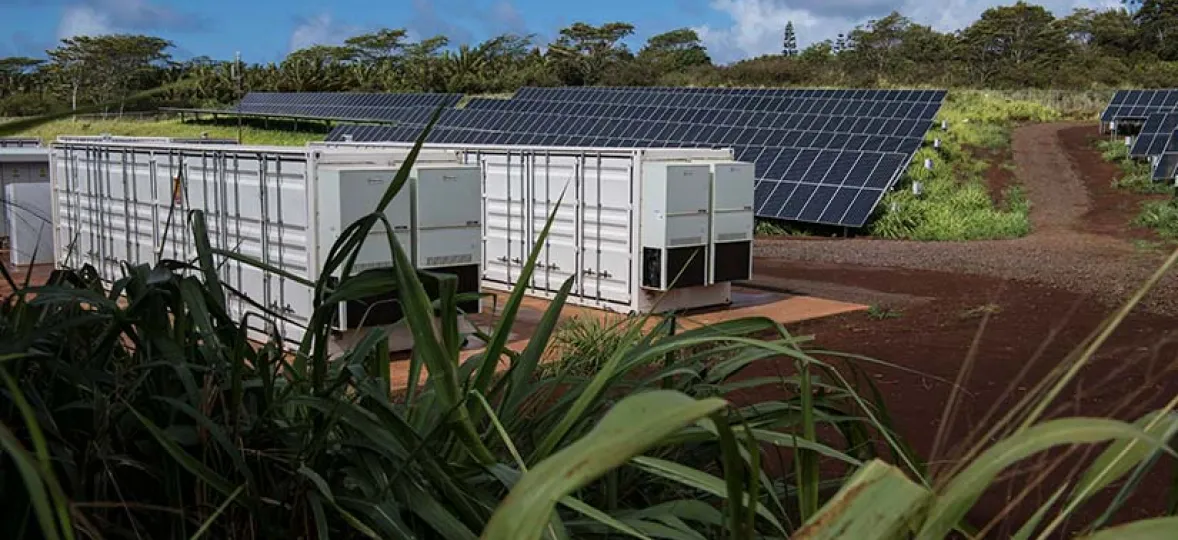 Solar panels and white storage containers in a grassy area under a blue sky.