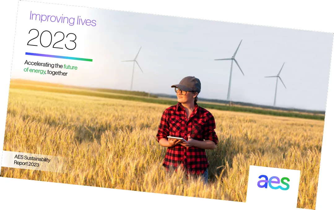 A person in a red plaid shirt and cap stands in a wheat field holding a tablet, with wind turbines in the background. Text reads: 'Improving lives 2023. Accelerating the future of energy, together. AES Sustainability Report 2023.' The AES logo is in the bottom right corner.