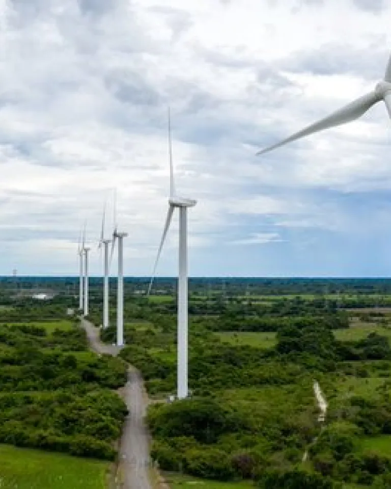 A row of wind turbines in a green landscape under a cloudy sky, generating renewable energy.