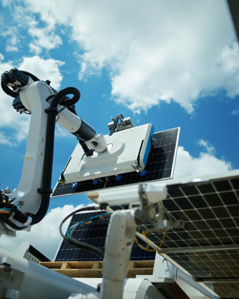 A robotic arm cleaning solar panels under a bright blue sky with scattered clouds.