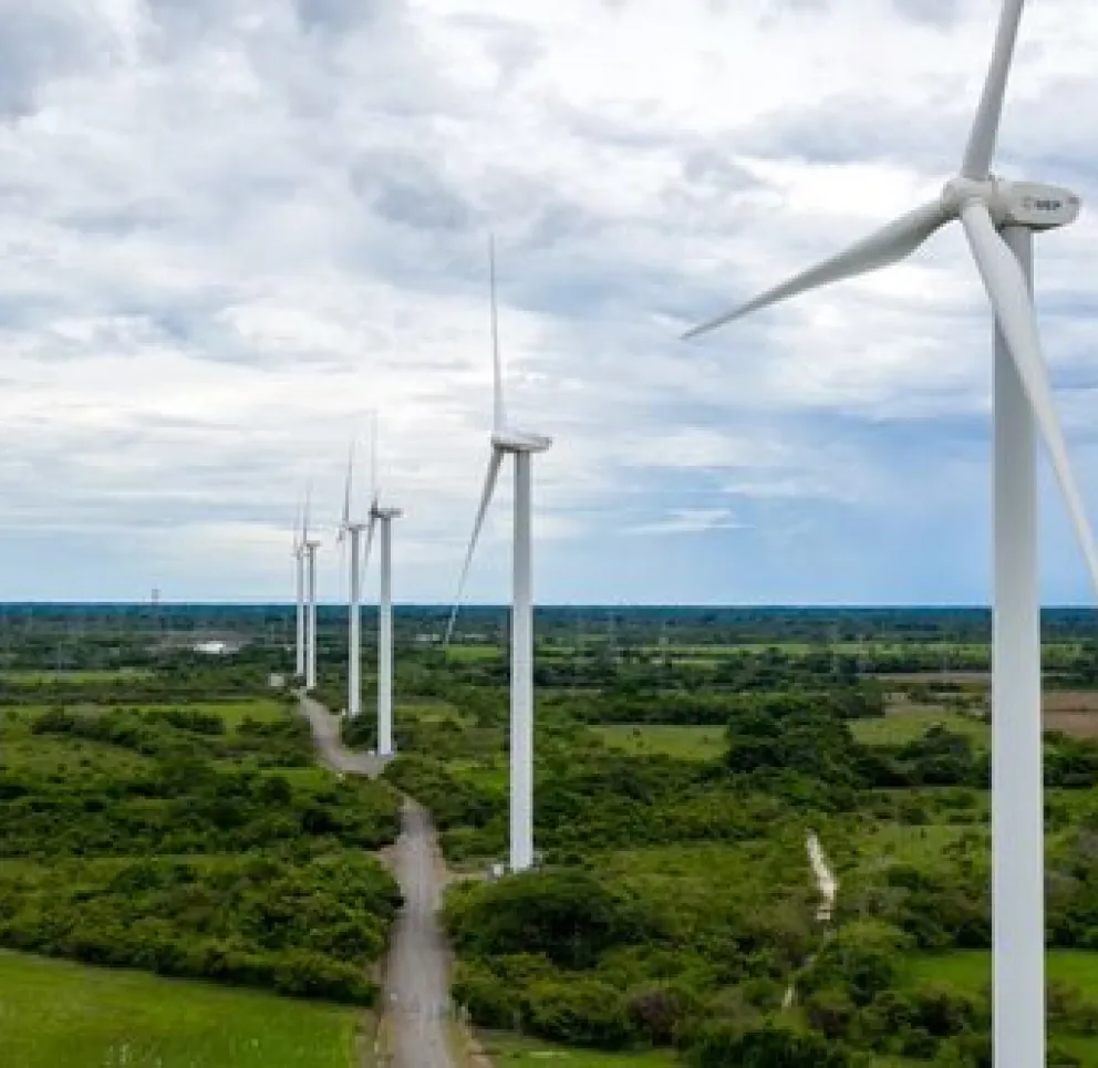 A row of wind turbines in a green landscape under a cloudy sky, generating renewable energy.