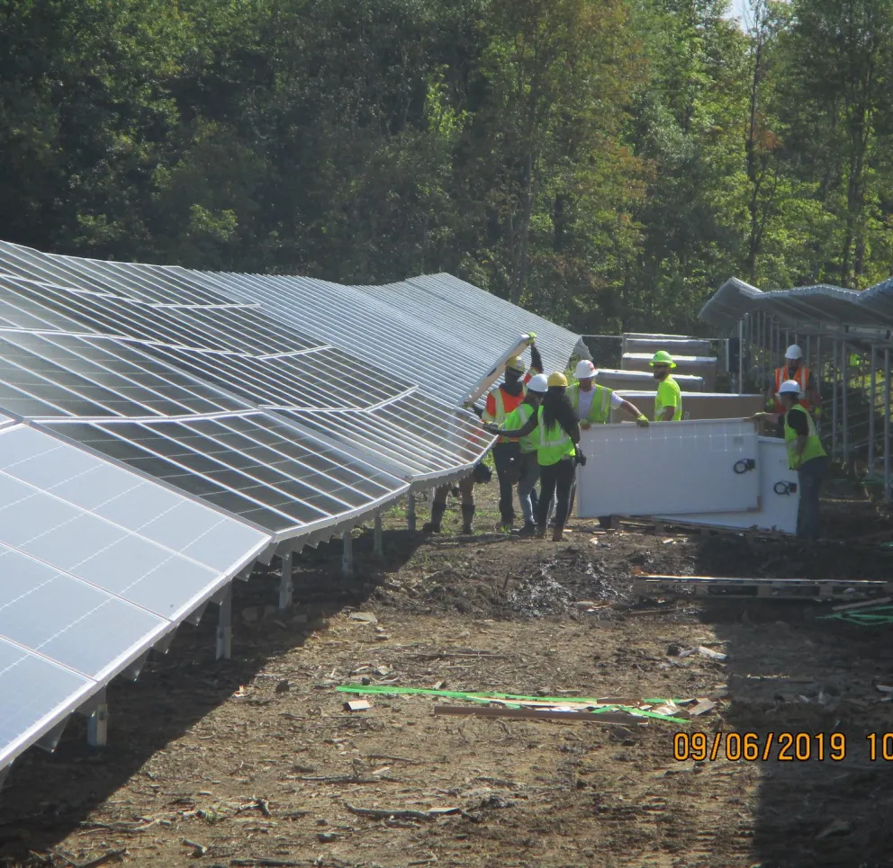 Workers in safety gear installing solar panels in a field with trees in the background.