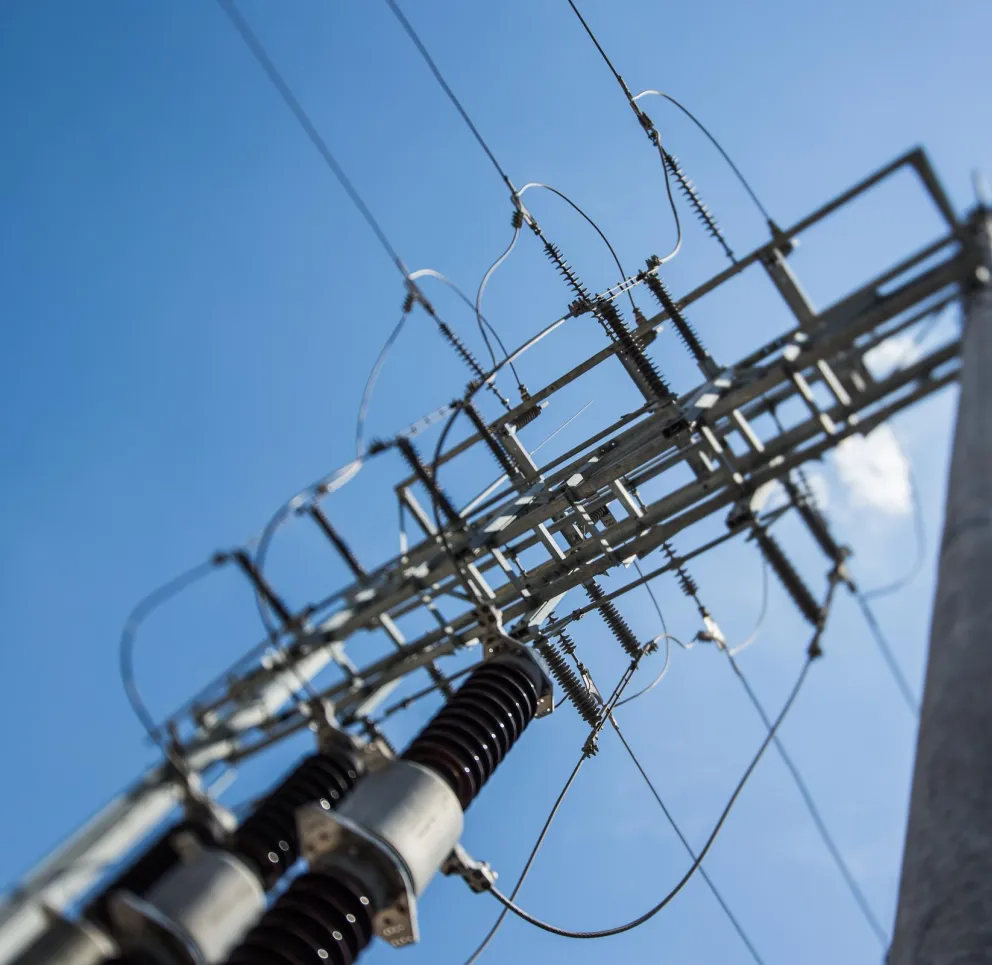 Close-up view of electrical power lines and insulators against a clear blue sky.