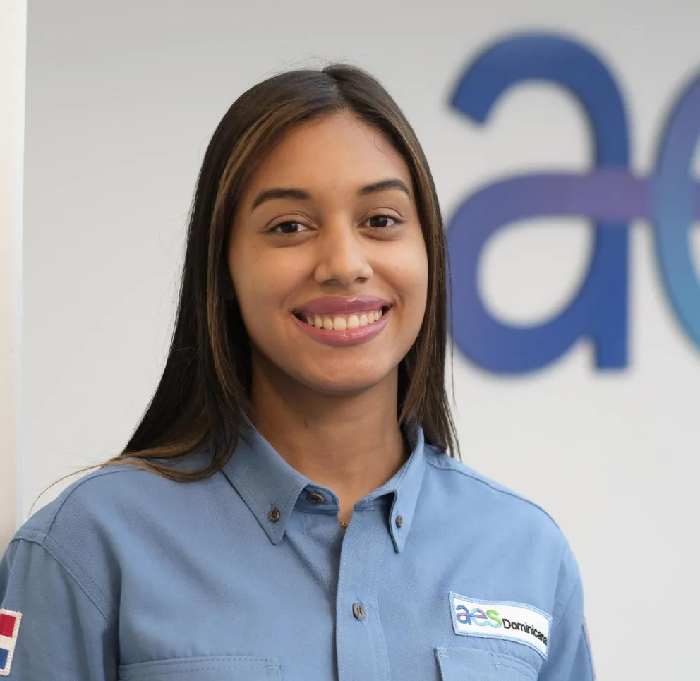 A person smiling, wearing a blue shirt with an AES Dominicana logo. The background shows a partial AES logo.