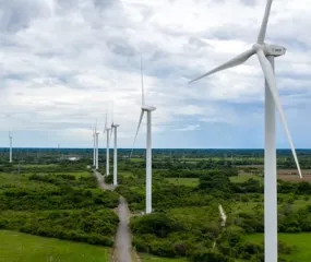 A row of wind turbines in a green landscape under a cloudy sky, generating renewable energy.