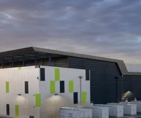 Modern industrial building with a geometric facade featuring green and gray accents, surrounded by rows of white utility cabinets, photographed at sunset under a cloudy sky.