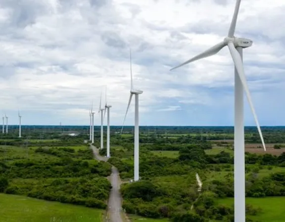 A row of wind turbines in a green landscape under a cloudy sky, generating renewable energy.