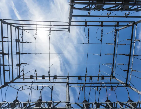 View from below of an electrical substation structure with metal beams, insulators, and wires against a blue sky with scattered clouds.