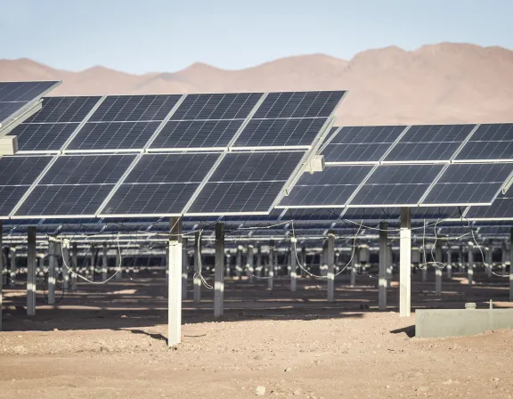 Rows of solar panels in a desert landscape with distant mountains under a clear blue sky.