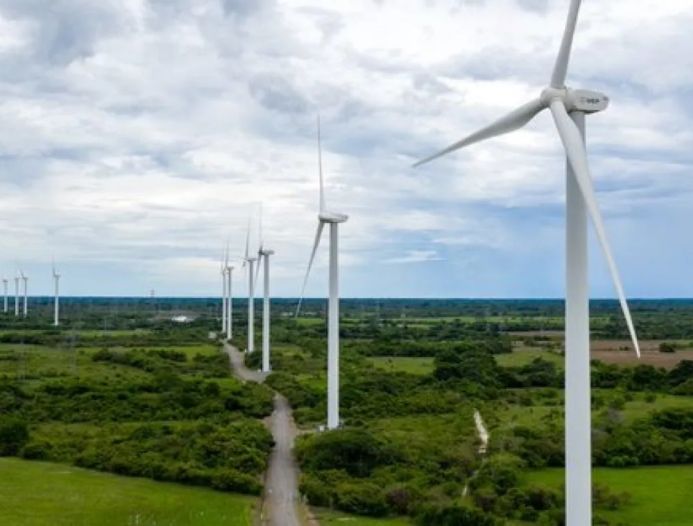 A row of wind turbines in a green landscape under a cloudy sky, generating renewable energy.