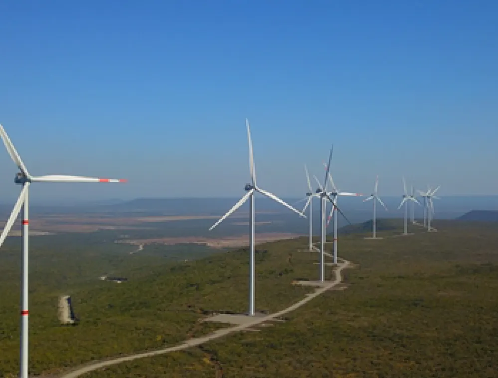 A row of wind turbines on a green landscape under a clear blue sky.