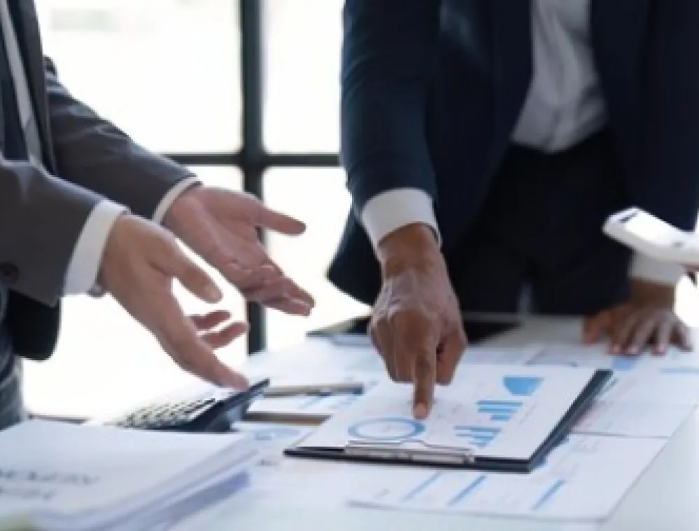 Business professionals discussing charts and graphs on a table, with one person pointing at a document.