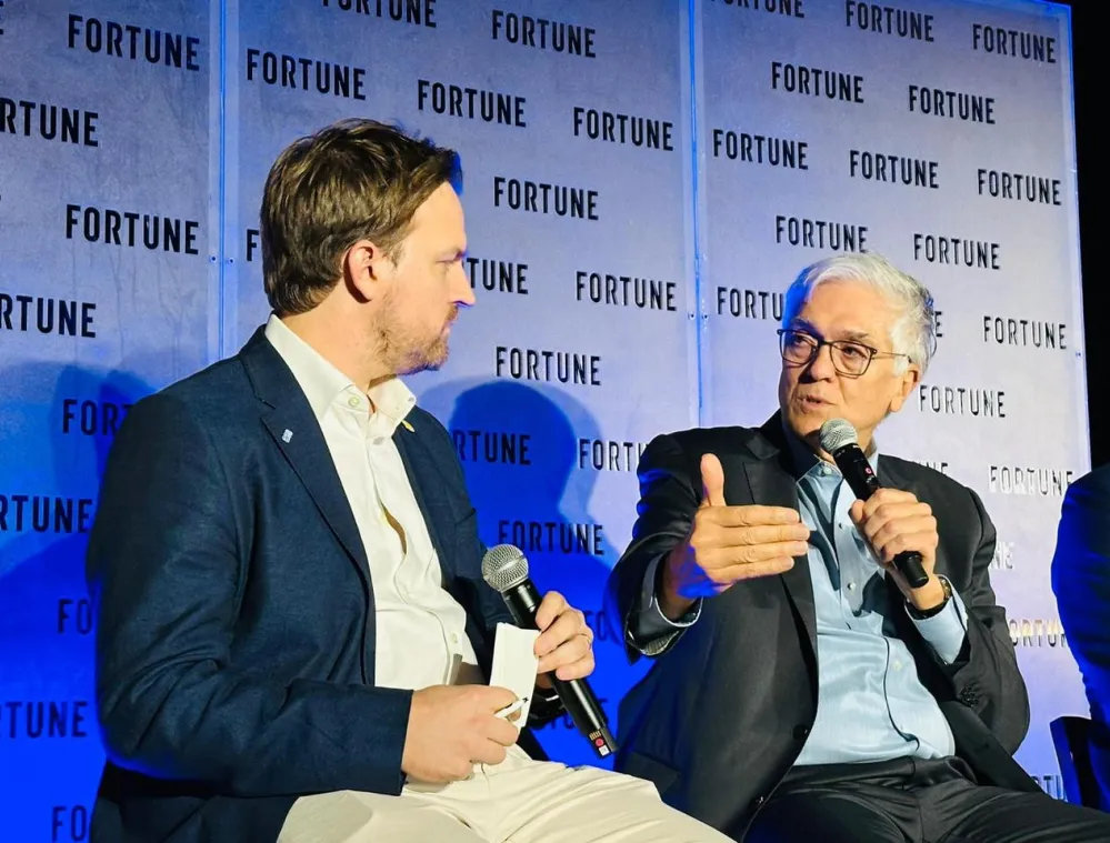Two men seated and speaking on stage at a Fortune event, holding microphones. The background displays the Fortune logo repeatedly.