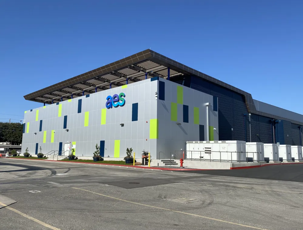 A modern industrial building with a colorful facade featuring blue and green panels, marked with the letters 'aes'. The structure is set against a clear blue sky.