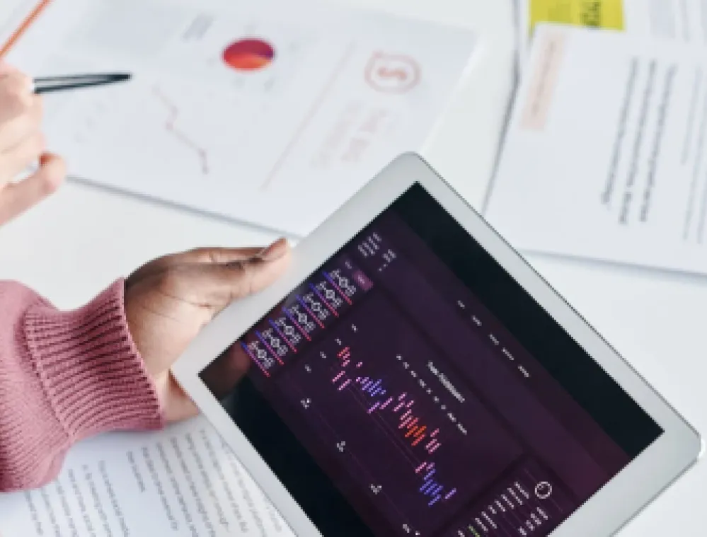 Two people reviewing financial charts on a tablet and printed documents on a desk.