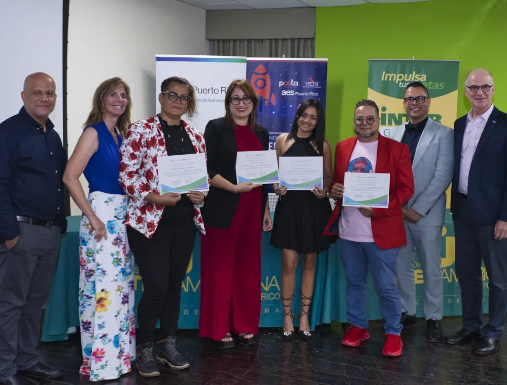 A group of people standing together indoors, some holding certificates, with banners in the background indicating a formal event.