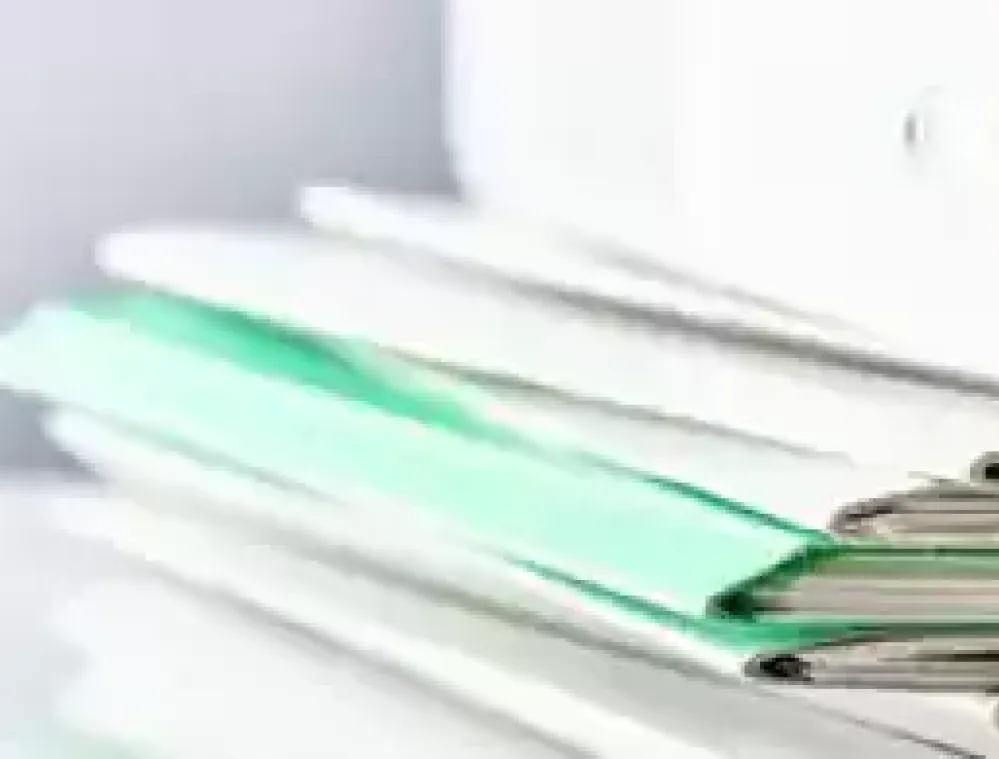 Stack of organized documents and folders in green and white on a desk, with a white binder in the background.