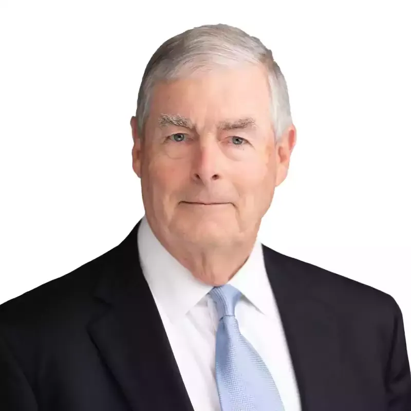 Portrait of an older man in a suit and light blue tie against a white background.