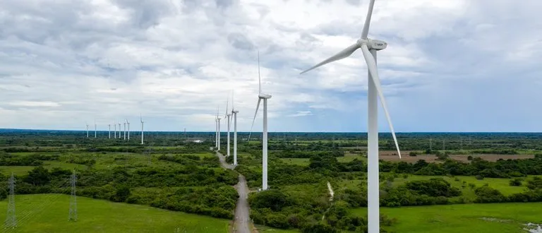 A row of wind turbines in a green landscape under a cloudy sky, generating renewable energy.