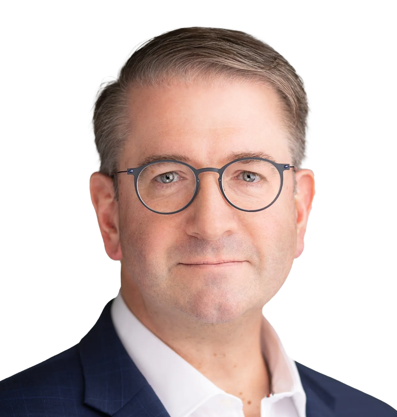 Professional headshot of Chris Shelton with short light brown hair, wearing round eyeglasses, a navy blue suit, and a white shirt, posing against a plain light background.