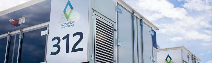A close-up view of an Advancion Energy Storage unit with the number 312 displayed prominently. The unit features a logo and ventilation panels. The sky is partly cloudy in the background.
