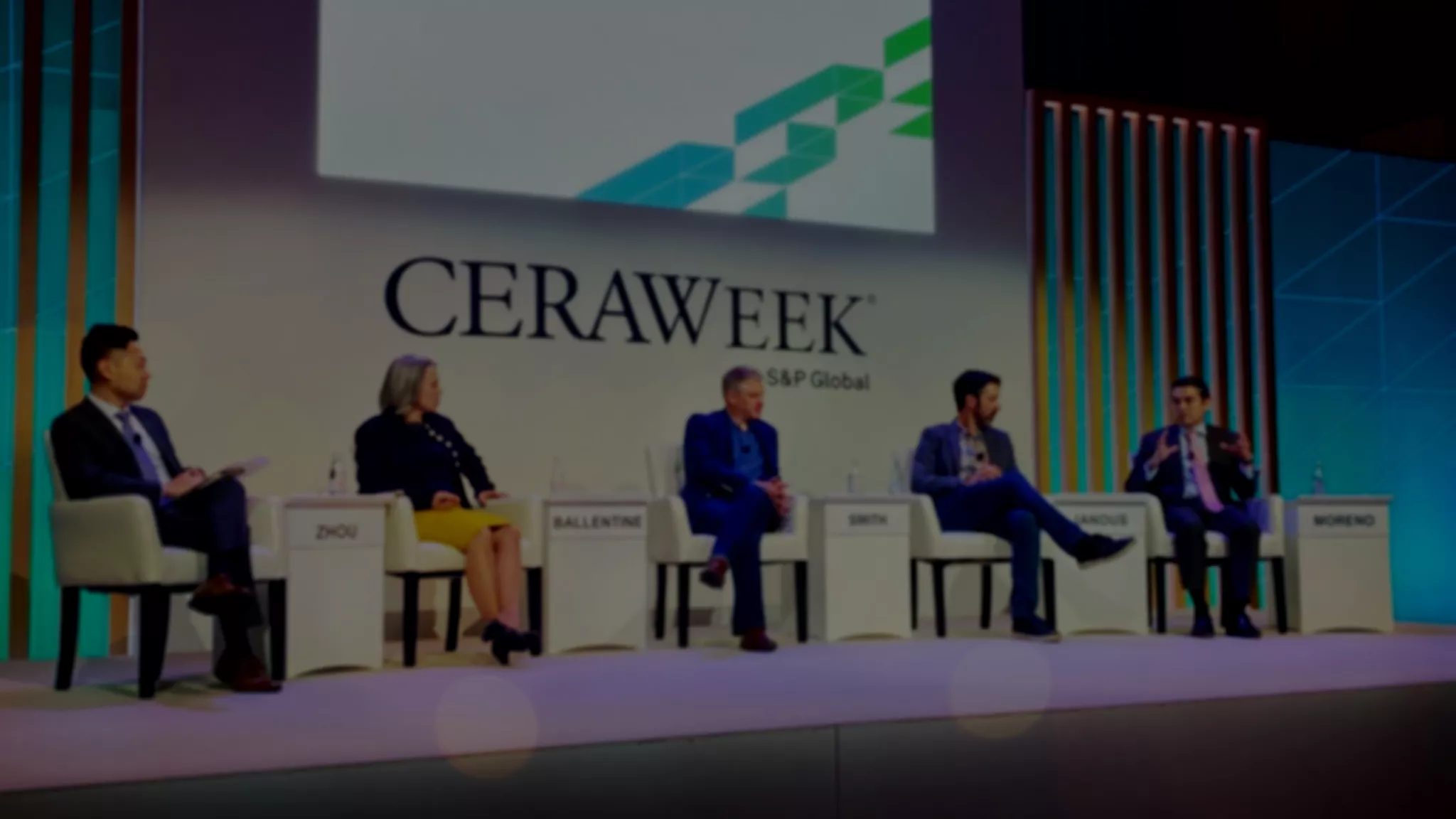 Five people sit on a panel stage at CERAWeek by S&P Global. They are seated in chairs with nameplates: Zhou, Ballentine, Smith, Manous, and Moreno. The backdrop features the CERAWeek logo and geometric designs. The panelists are engaged in discussion, with one speaking and others listening.