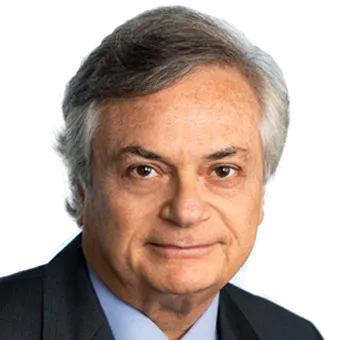Portrait of an older man with gray hair wearing a dark suit and blue shirt, looking directly at the camera.