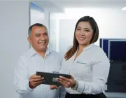 Two people in white shirts smiling and holding a tablet in an office environment.